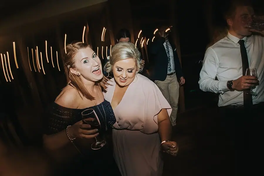 Two women embracing on the dance floor under golden streaks of light.
