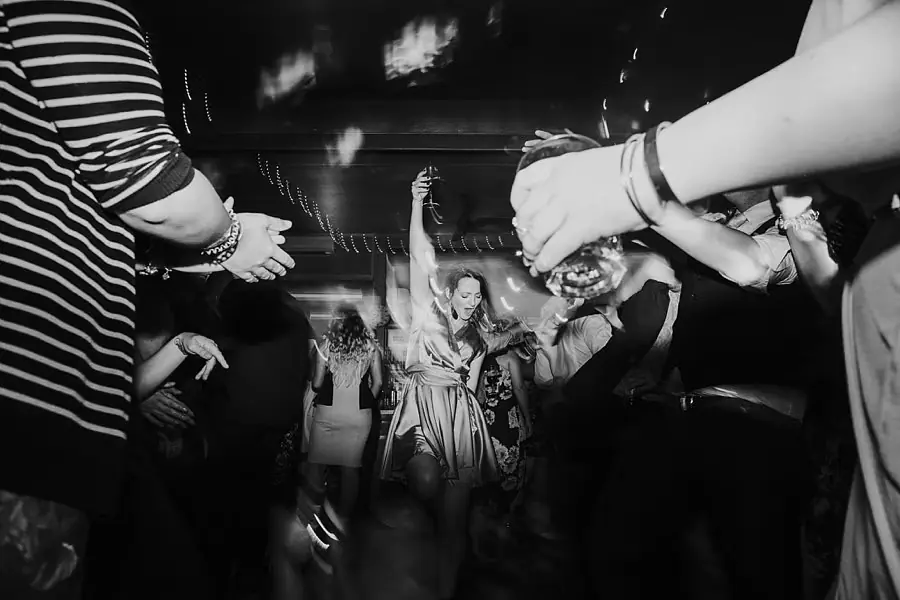 Black-and-white photograph of guests dancing with raised arms.