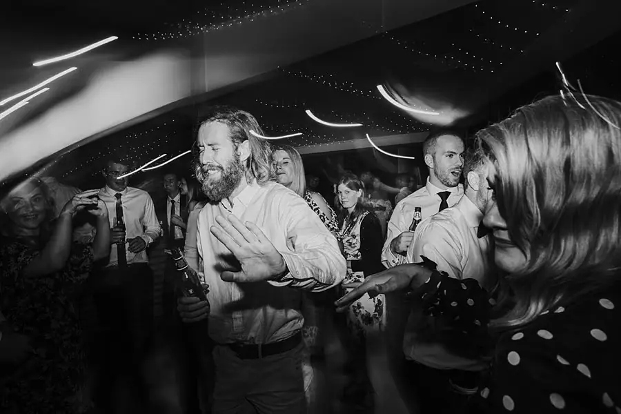 Black-and-white photograph of guests dancing beneath streaks of light.