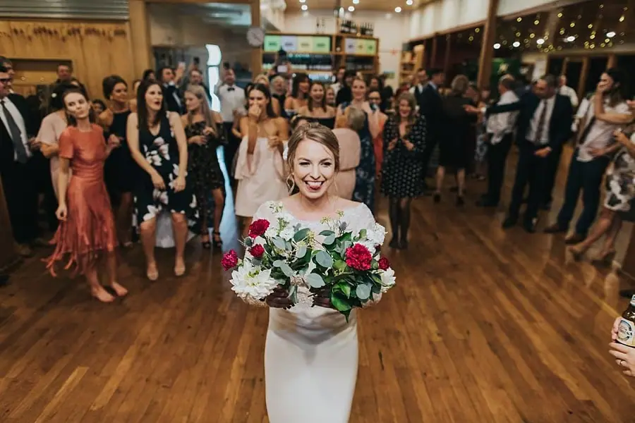 Bride holding her bouquet in front of guests gathered on the dance floor.