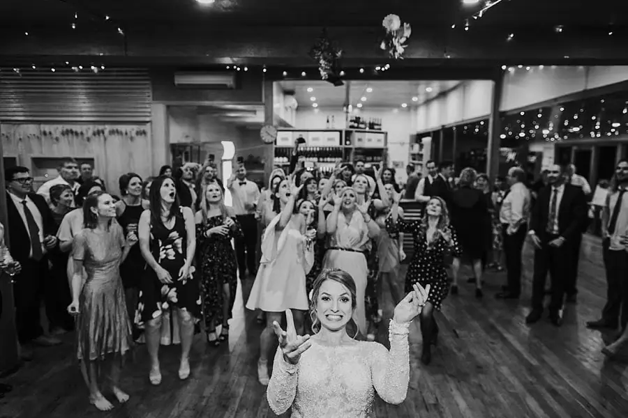 Black-and-white photograph of the bride tossing her bouquet toward guests.