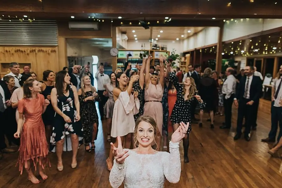 Bride smiling after throwing her bouquet while guests reach behind her.