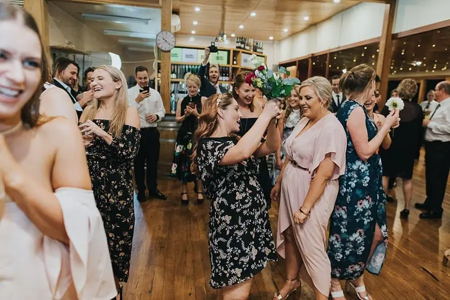 Women laughing together with the caught bouquet on the dance floor.