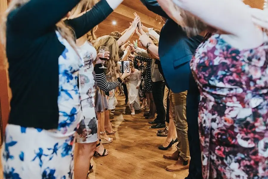 Guests holding hands overhead to form an arch across the reception floor.