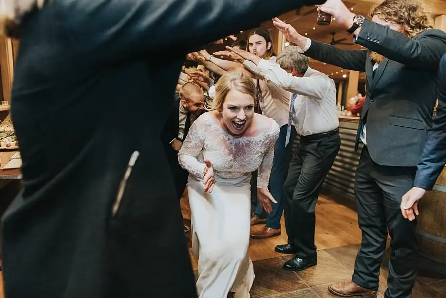 Bride laughing as she ducks beneath an arch formed by guests' raised hands.