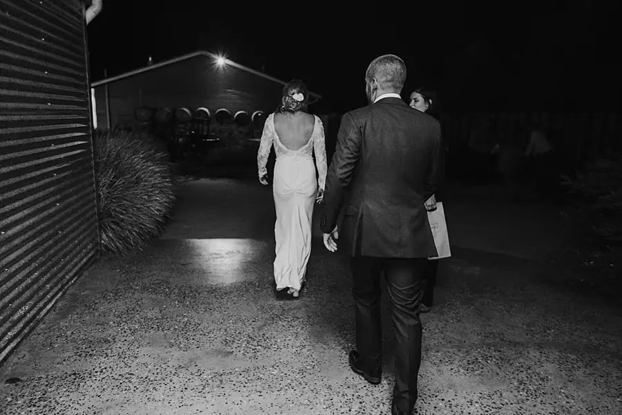 Black-and-white photograph of the bride and groom walking away outside at night.