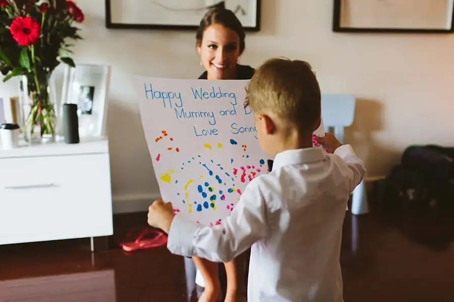 Young boy presenting a colourful handmade wedding card to the smiling bride