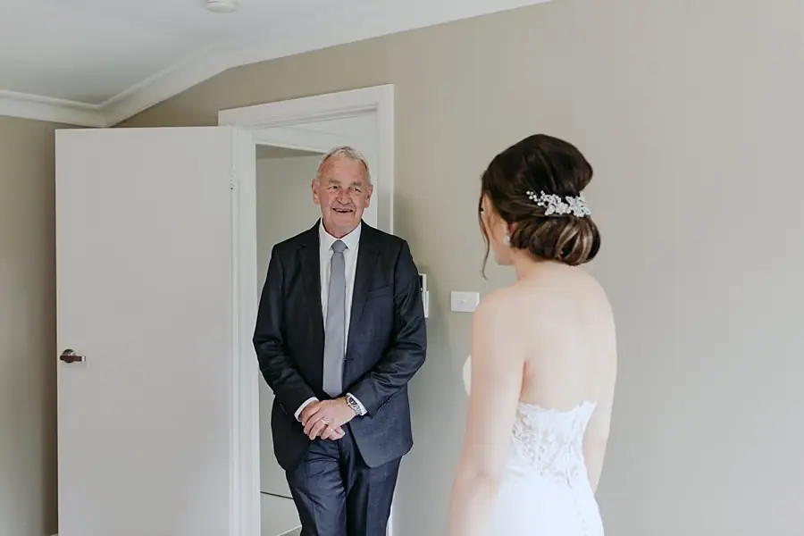 Older man looks at the bride through an open doorway indoors.