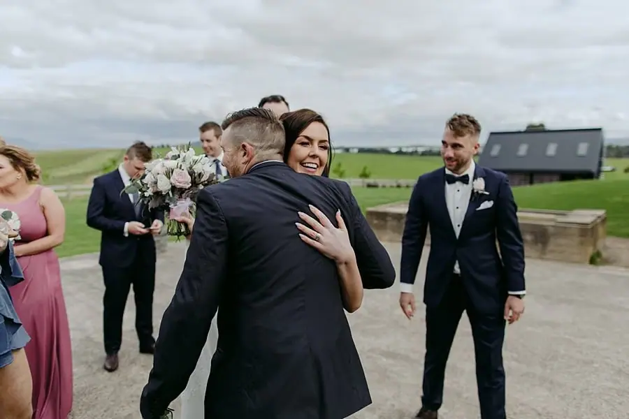 Bride laughs as she hugs a guest outside.