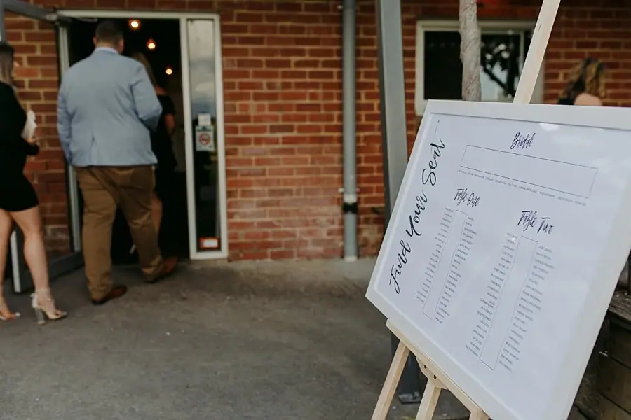 Seating chart on an easel beside guests entering the brick-walled venue.