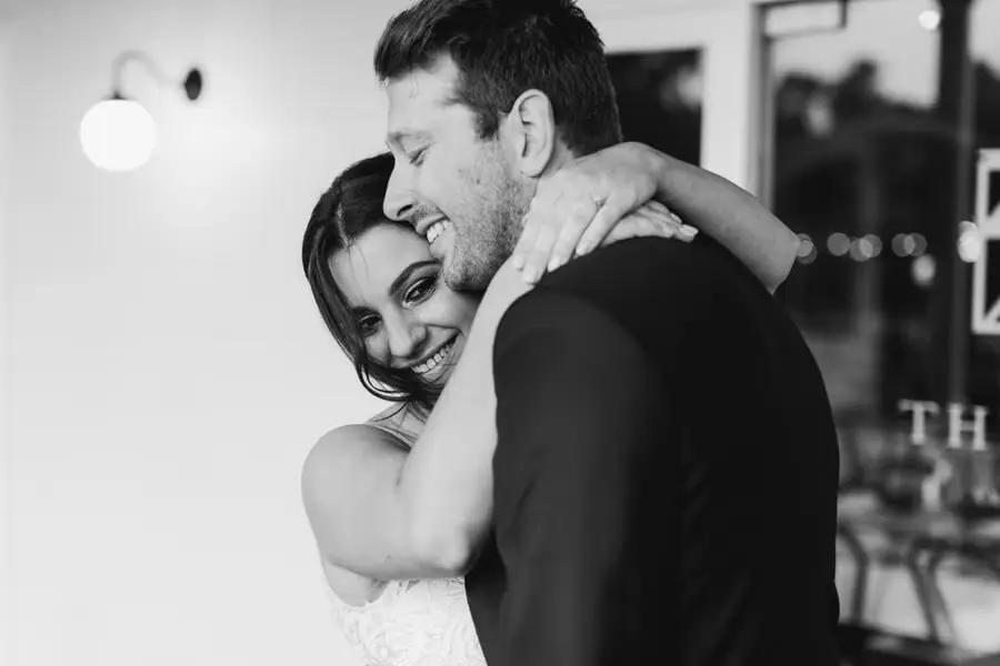 Black-and-white photograph of the smiling bride embracing the groom indoors.