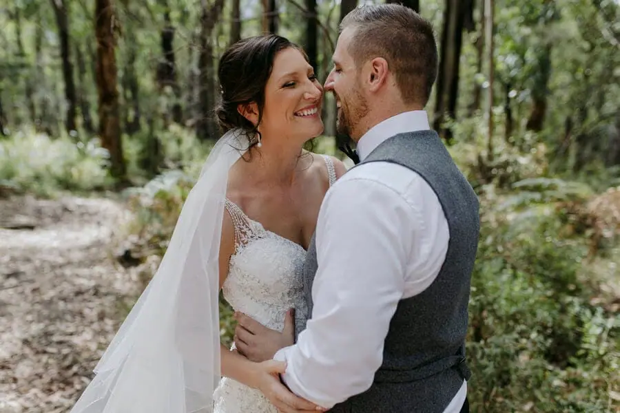 Bride and groom smiling at each other among forest trees.