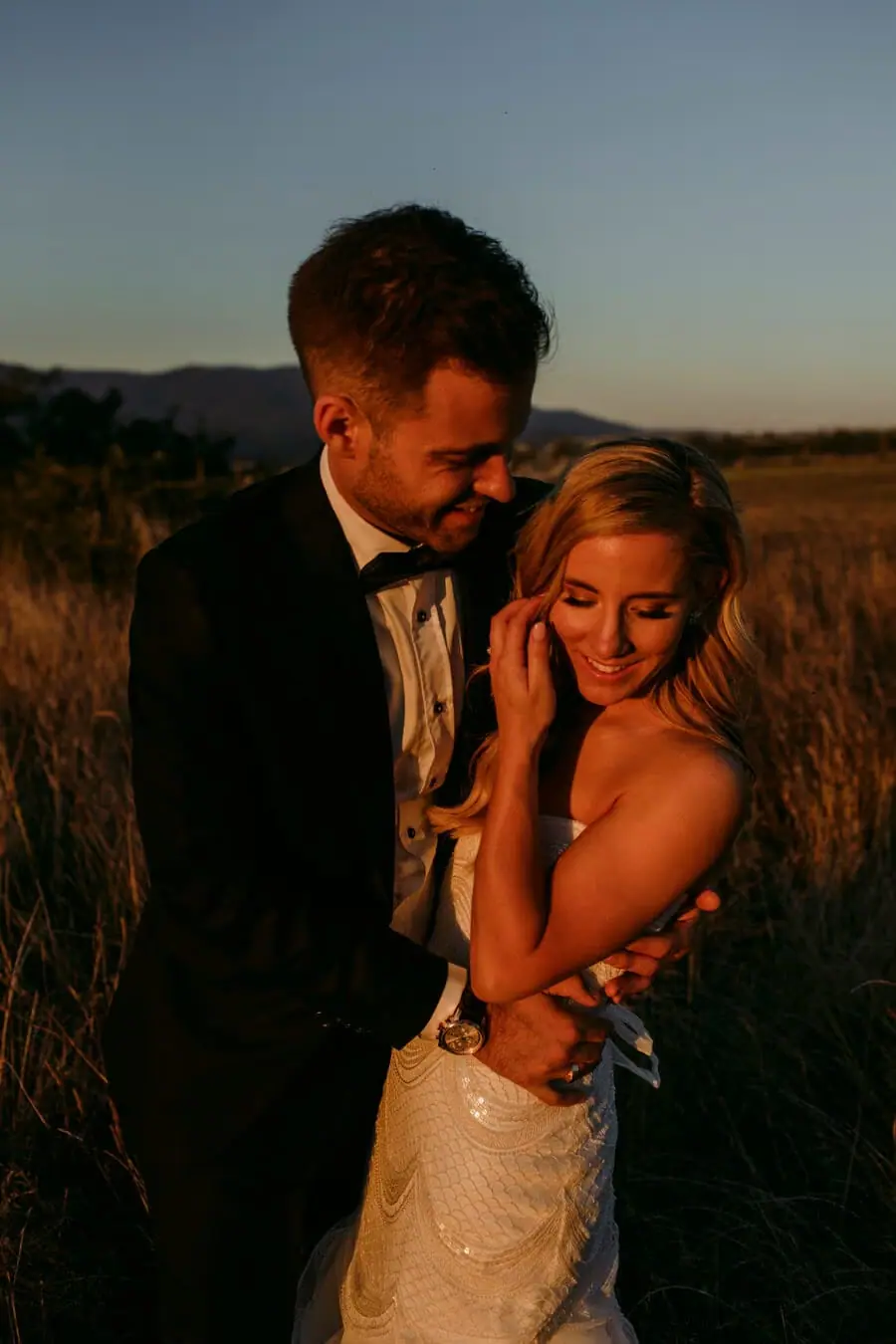 Couple standing close together in warm evening light in a field.