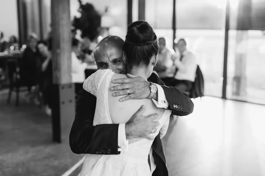 Black-and-white photograph of the bride hugging a man indoors.