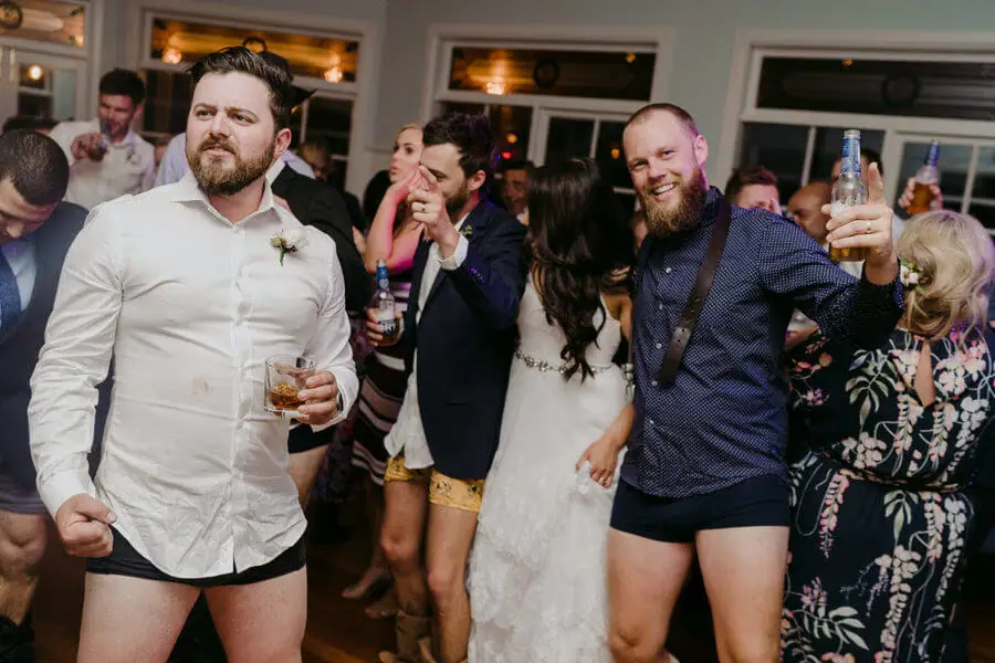 Guests in shirts and underwear laughing and holding drinks at a reception.