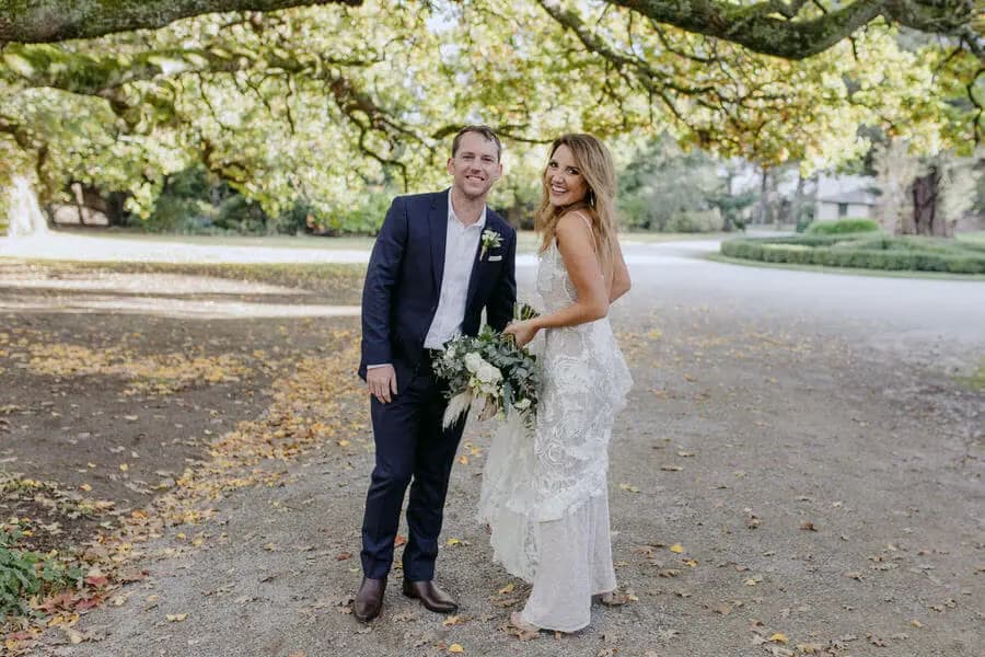 Couple posing beneath a broad leafy tree beside a quiet road.