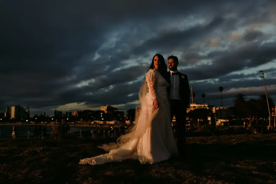 Couple standing beneath dark dramatic clouds above a waterfront town.
