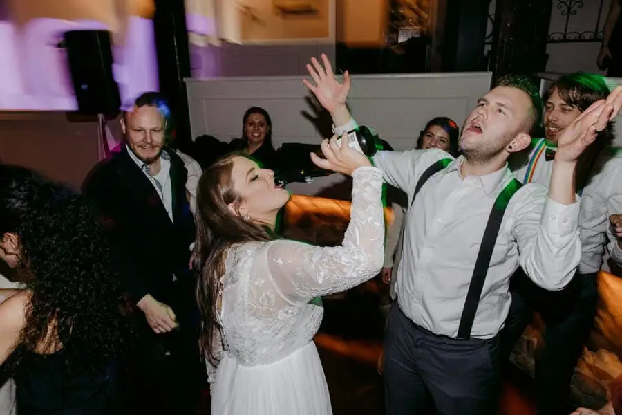 Bride holding a bottle toward a laughing man's mouth on the dance floor.