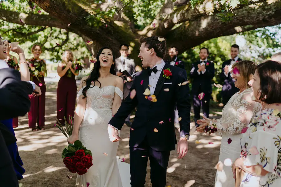 Couple walking through colourful petals beneath a large tree.