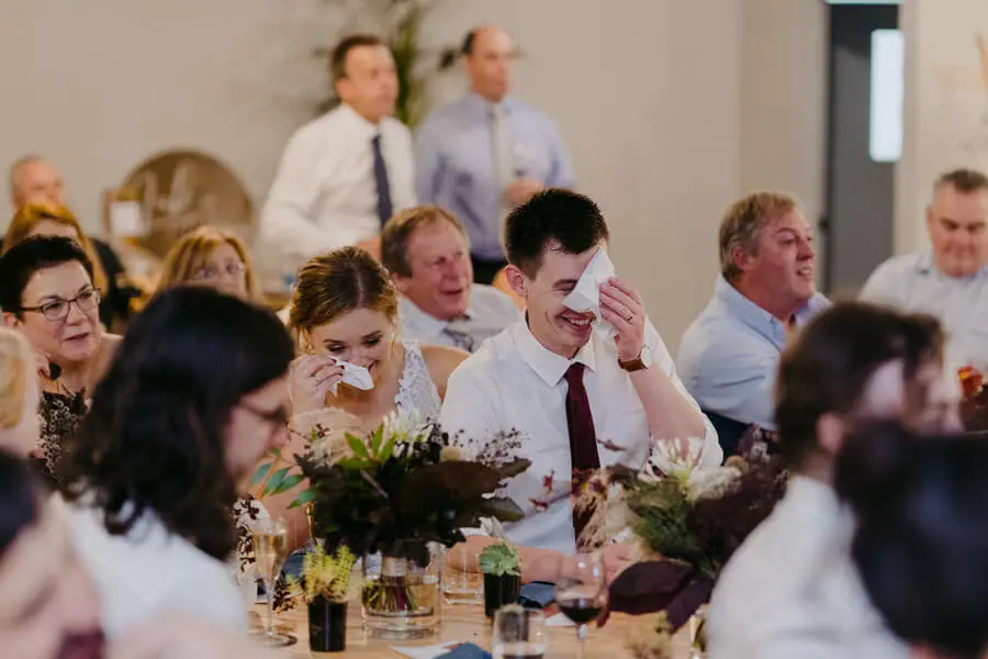 Guests laughing together at a flower-decorated reception table.