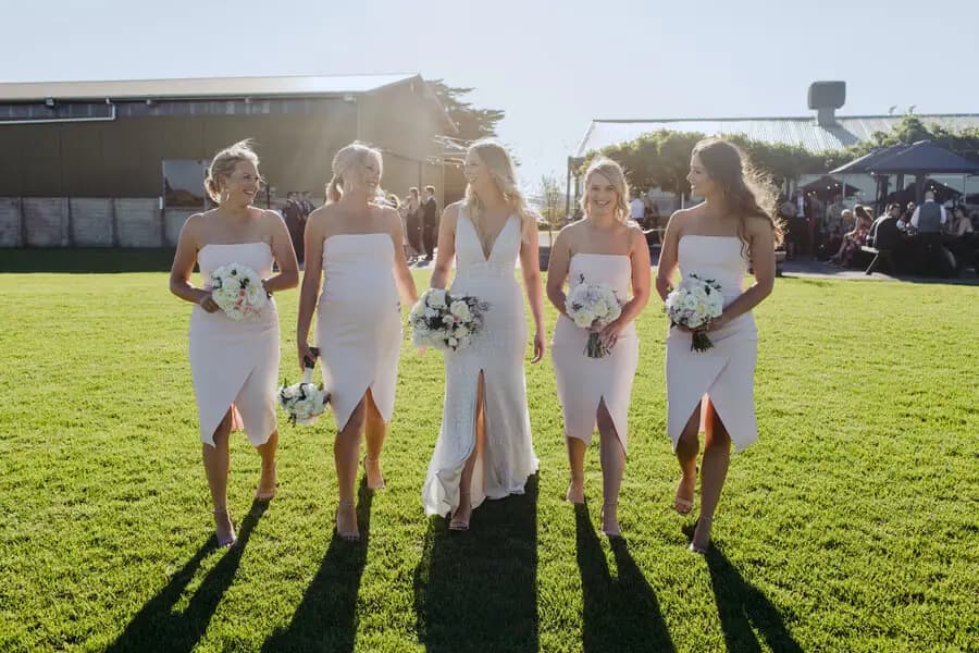 Bride and four women holding white bouquets on a sunny lawn.
