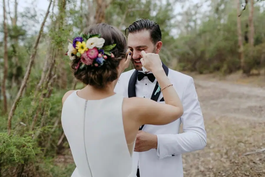 Bride touching the groom's face on a woodland path.