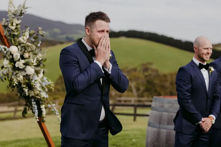 Groom covering his mouth with both hands beside the ceremony flowers.