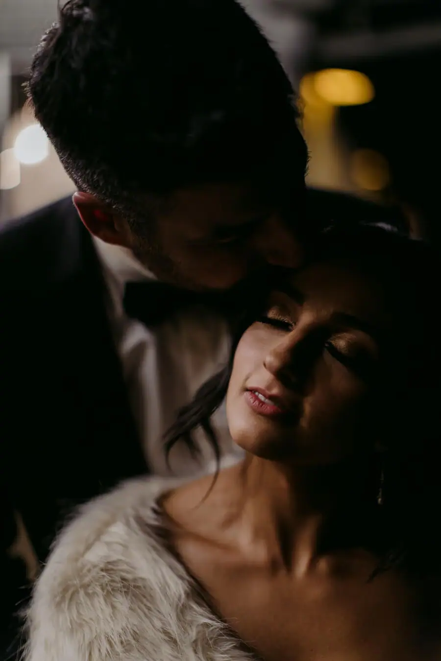 Close portrait of a couple embracing in soft dim light.