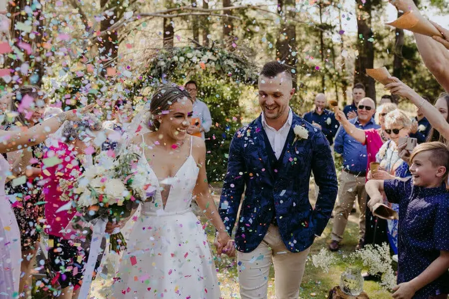 Couple walking through a shower of colourful confetti in woodland.