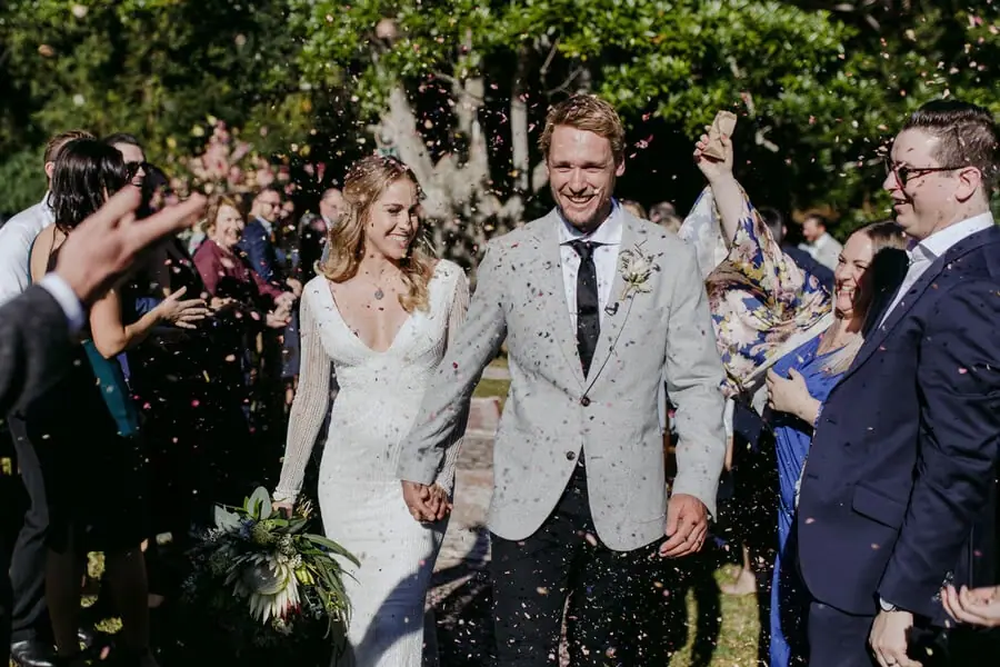 Bride and groom smiling under a shower of white petals.