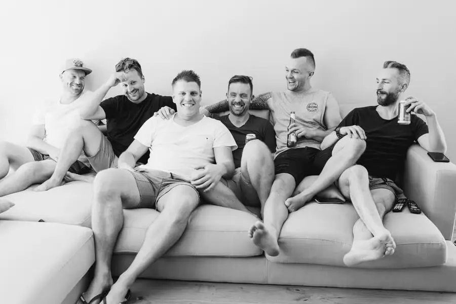 Black-and-white photograph of men laughing while seated together on a sofa.