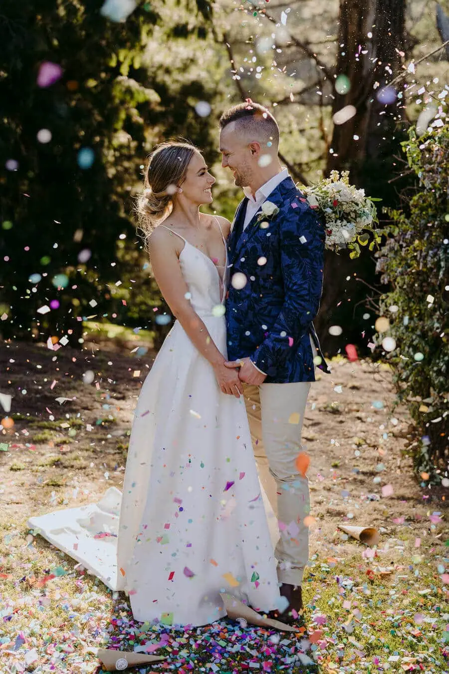 Couple kissing beneath falling colourful confetti in a garden.