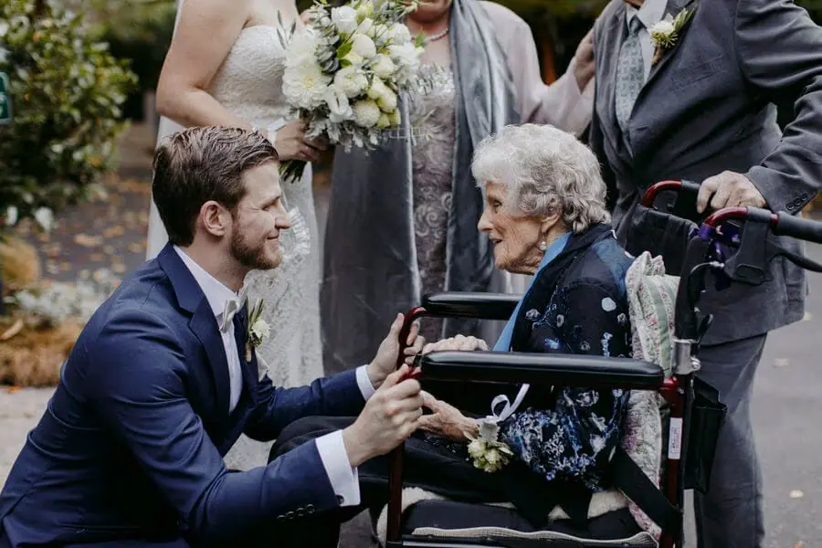 Man crouching and holding the hands of an older woman in a wheelchair.