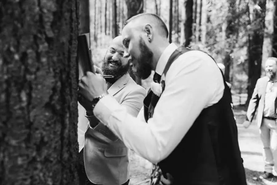 Black-and-white photograph of men laughing together among forest trees.