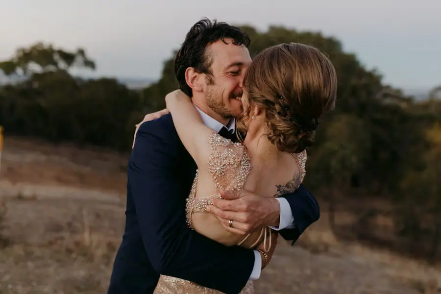 Couple kissing and embracing on a grassy hillside.