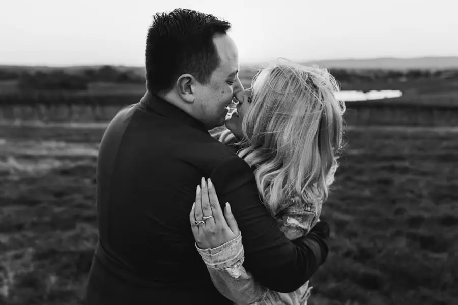 Black-and-white close portrait of a couple kissing in a field.