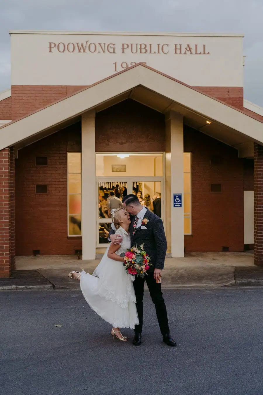 Bride and groom embracing outside a public hall.