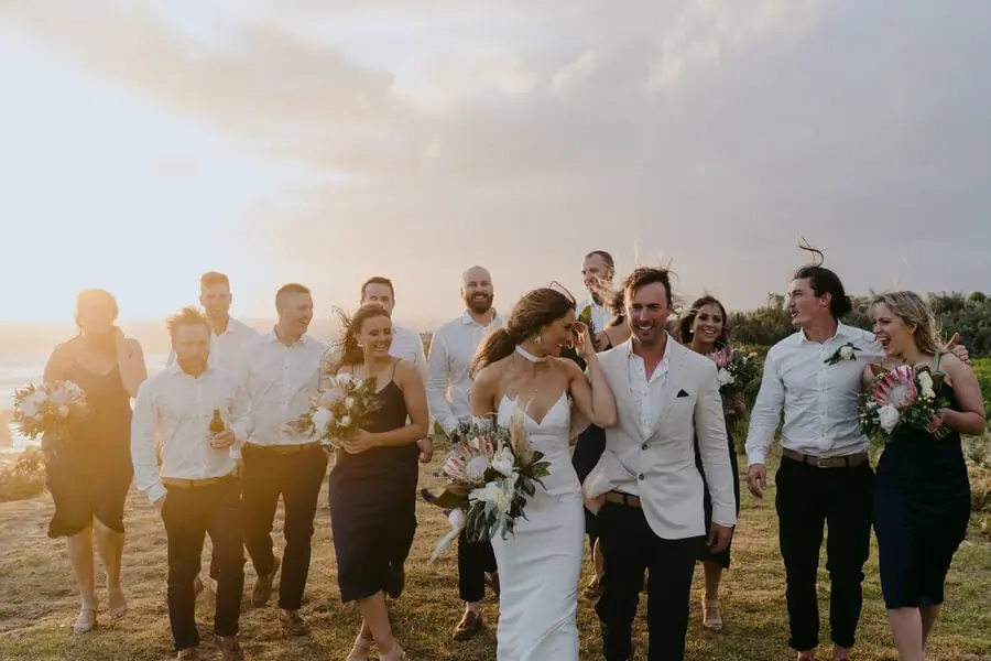 Wedding party walking together through a grassy field in sunset light.