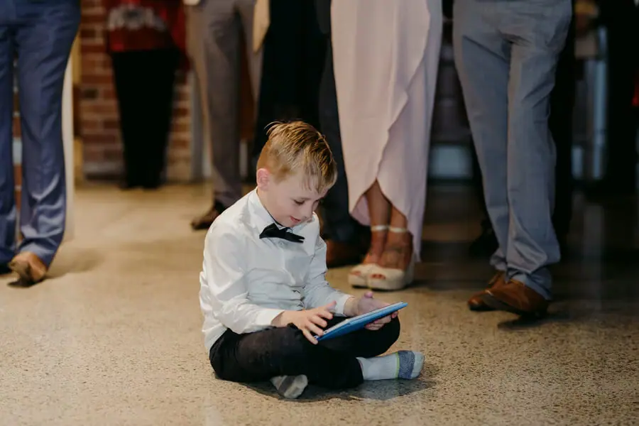 Small boy in a bow tie sitting on the floor and looking at a tablet.