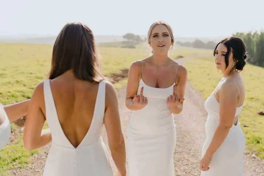 Three women in white dresses chatting beside a sunny field.