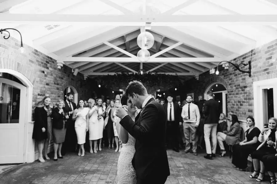 Black-and-white photograph of a couple dancing inside a brick reception room.