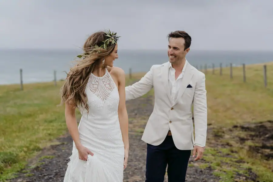Couple smiling beside the sea while wind blows the bride's hair.