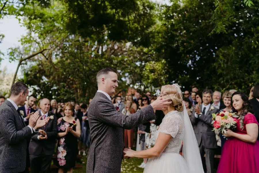 Groom reaching toward the bride's face during an outdoor ceremony.