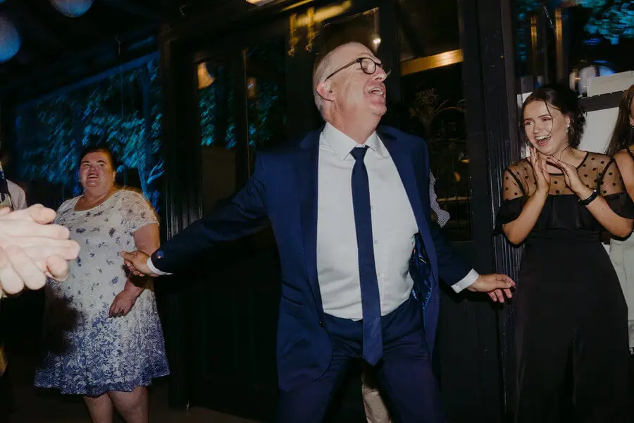 Man dancing with his arms spread among reception guests.