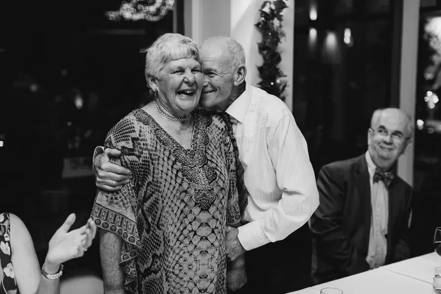 Black-and-white photograph of an older man kissing a laughing woman's cheek.
