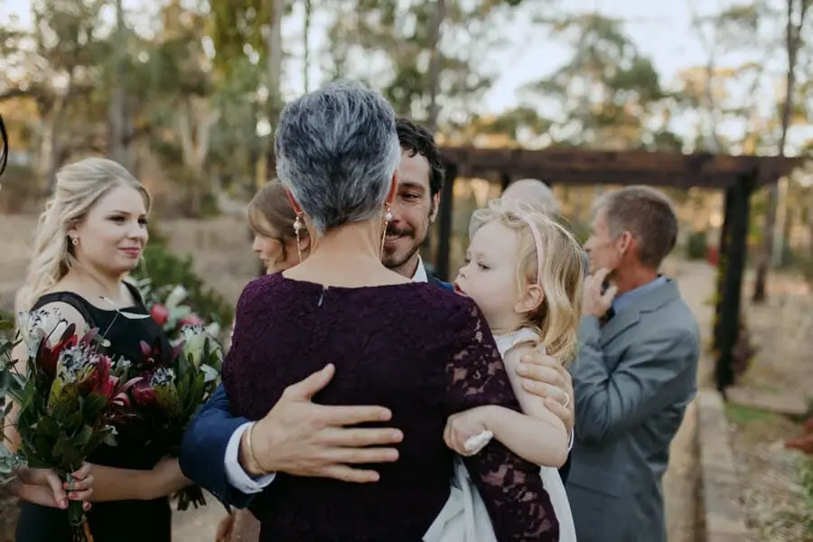 Man embracing a woman holding a young child after a woodland ceremony.