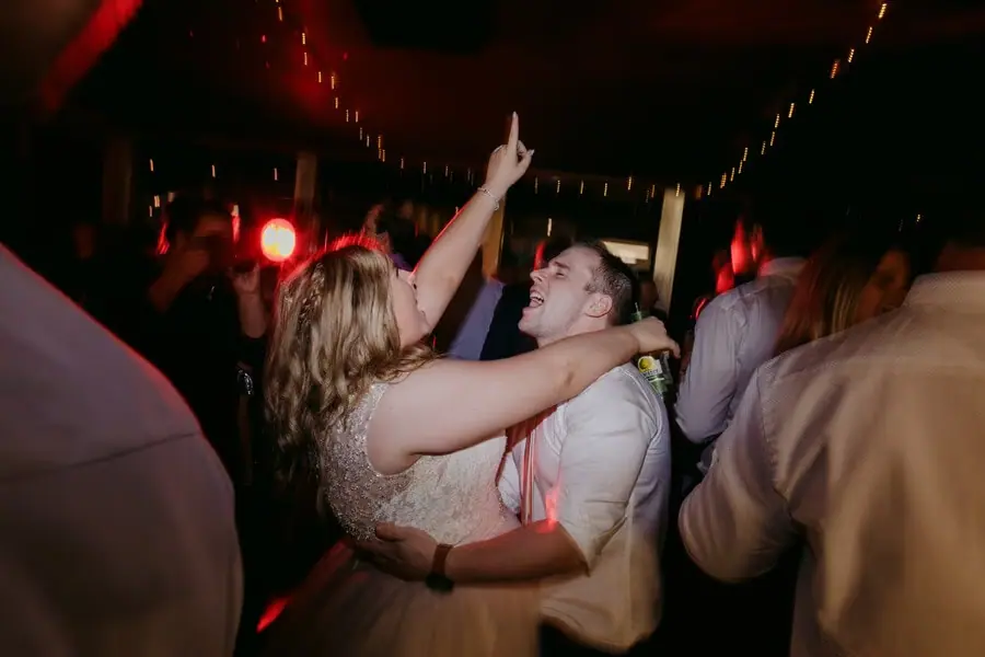Bride dancing closely with a man beneath red reception lights.