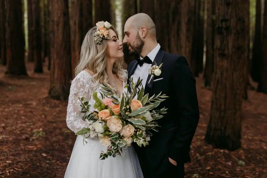 Bride and groom kissing among tall forest trees.