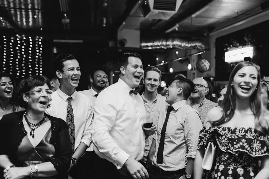 Black-and-white photograph of guests laughing and cheering at the reception.