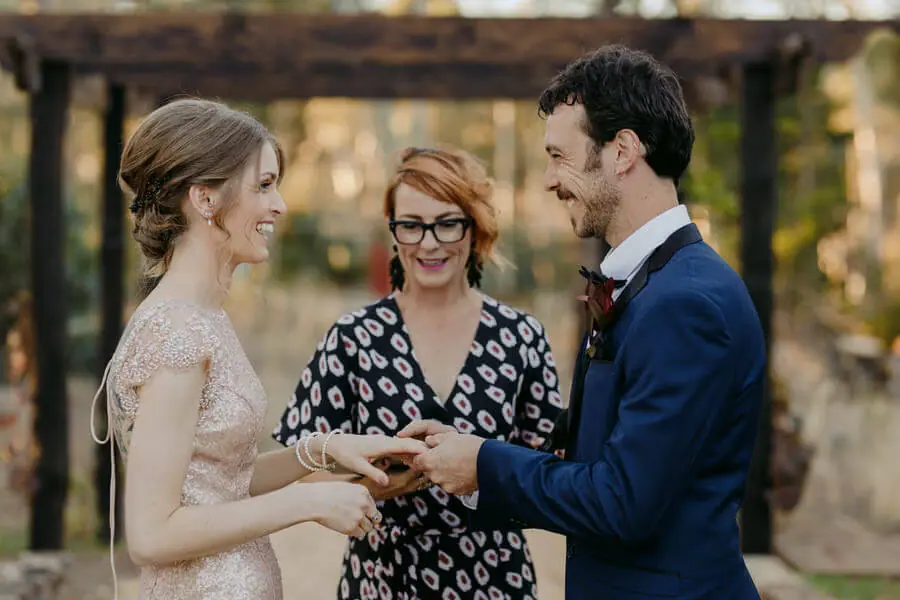 Couple exchanging rings beside a celebrant in woodland.